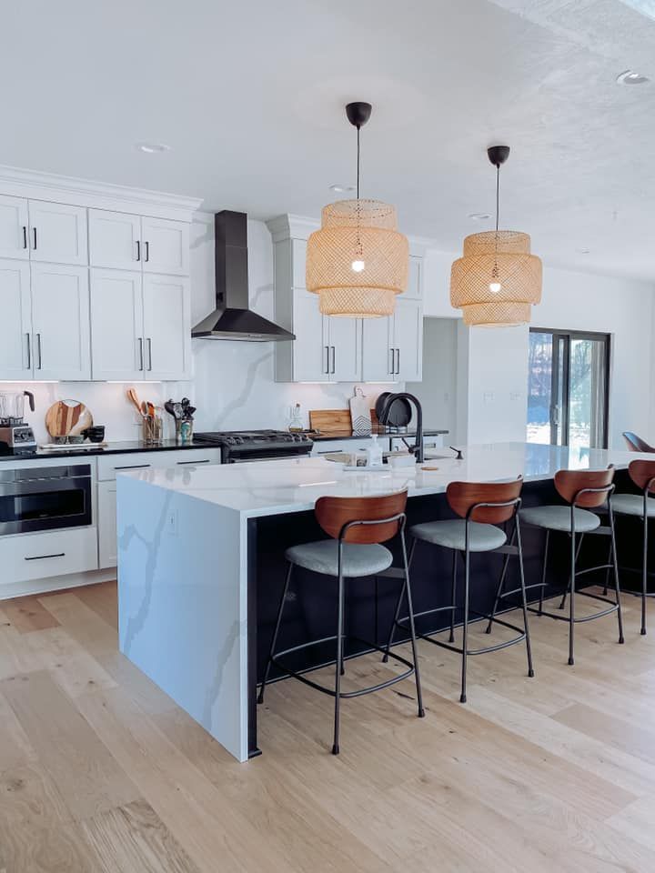 Modern kitchen with white cabinets, dark island with seating, and woven pendant lights.