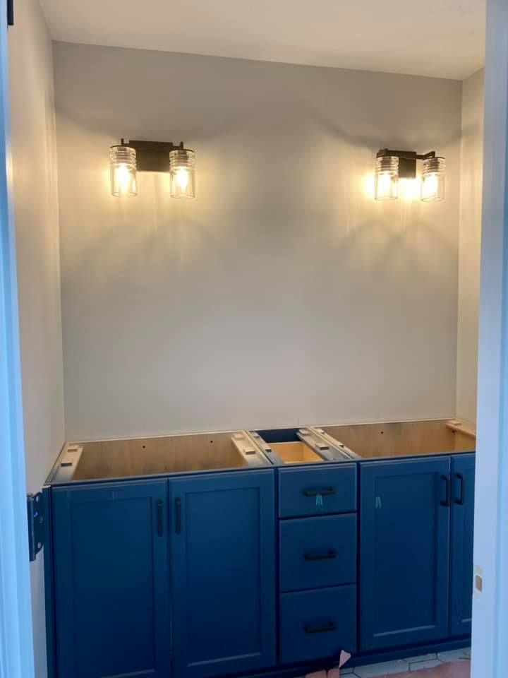 Bathroom with blue cabinets, two sconces on wall above, unfinished.