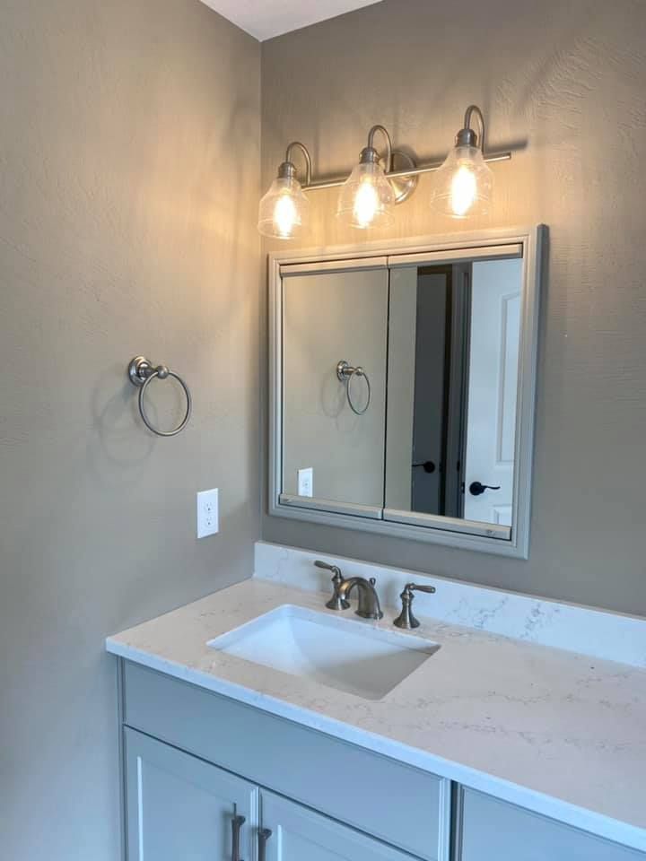 Bathroom with light gray vanity, white countertop, rectangular mirror, and three-bulb light fixture.