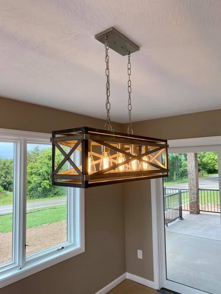 Rectangular farmhouse style chandelier suspended from a ceiling, above windows with an outdoor view.
