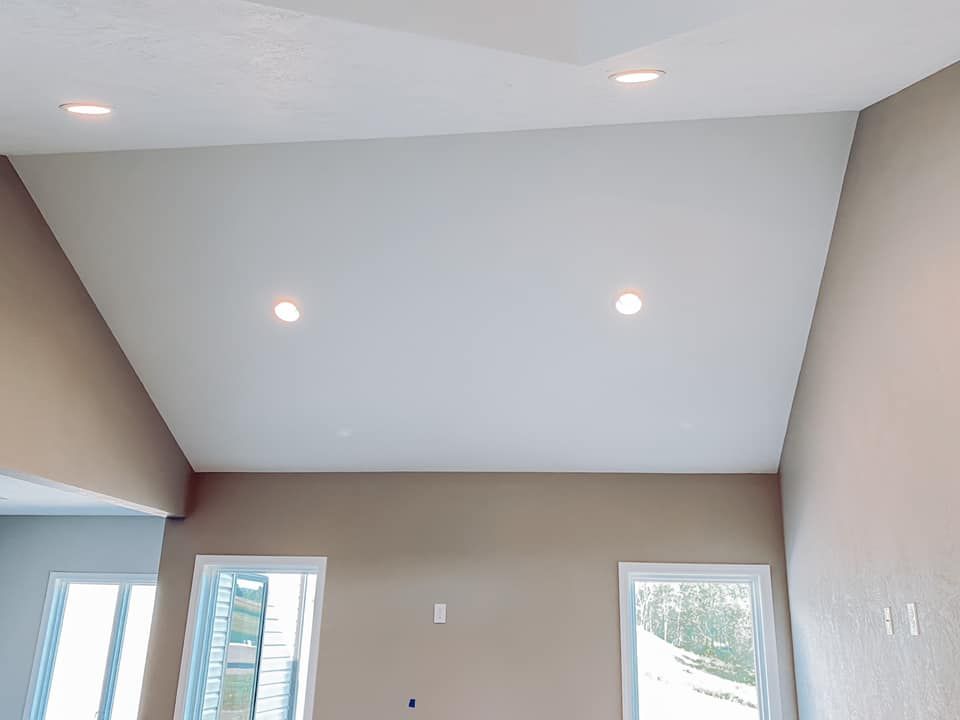 A high ceiling with recessed lights, above light brown walls and windows.