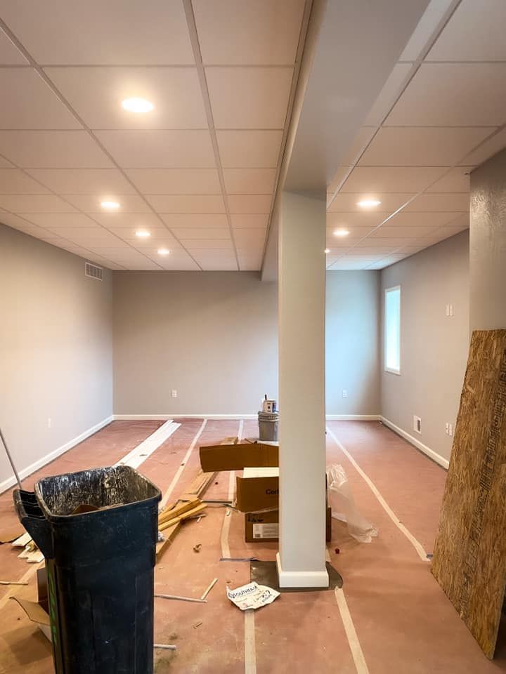 Basement renovation in progress; gray walls, white ceiling tiles, exposed pink flooring, debris.