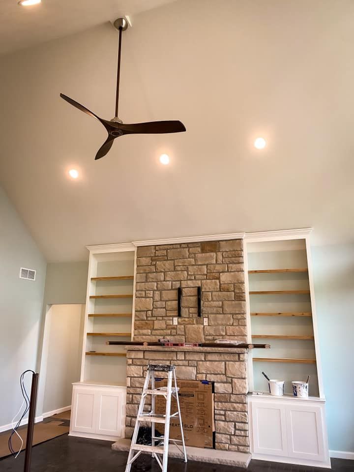 High-ceiling living room with stone fireplace, built-in bookshelves, ceiling fan, and recessed lighting.