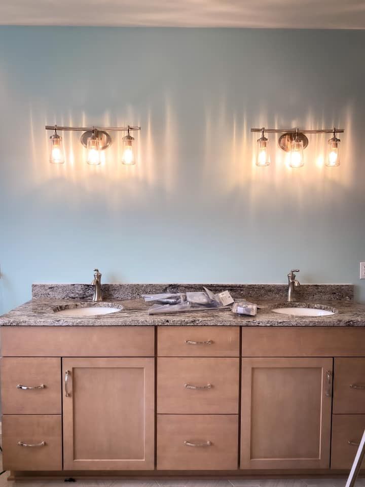 Two light fixtures above bathroom vanity with light brown cabinets and blue wall.