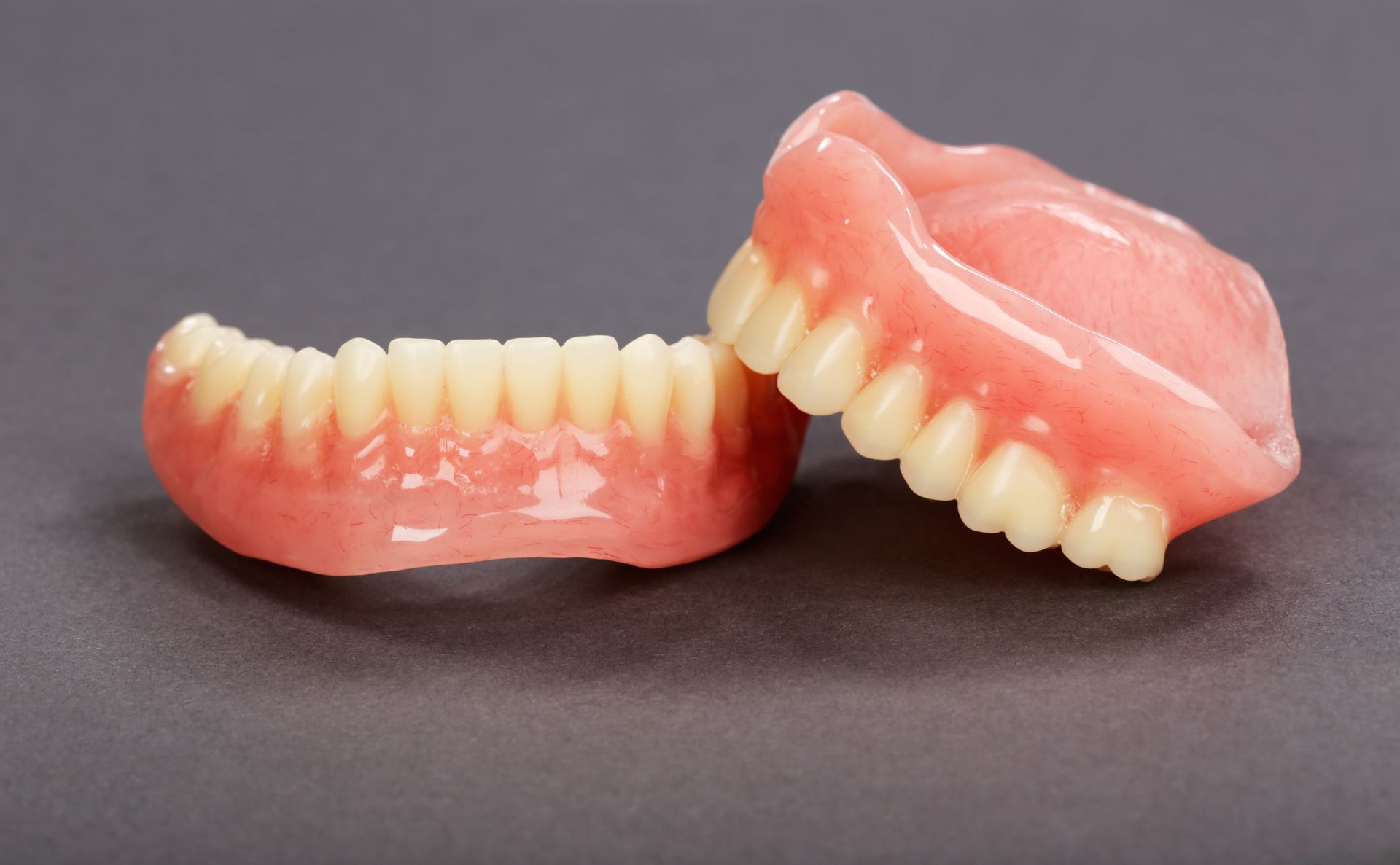 False teeth set, upper and lower dentures with pink gums and white teeth against a gray background.
