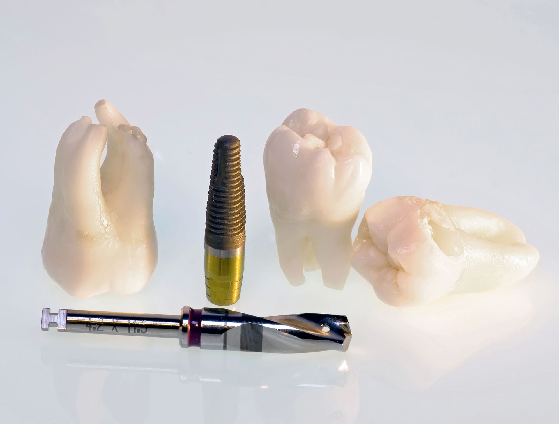 Dental implant and drill with three extracted teeth on a white surface.