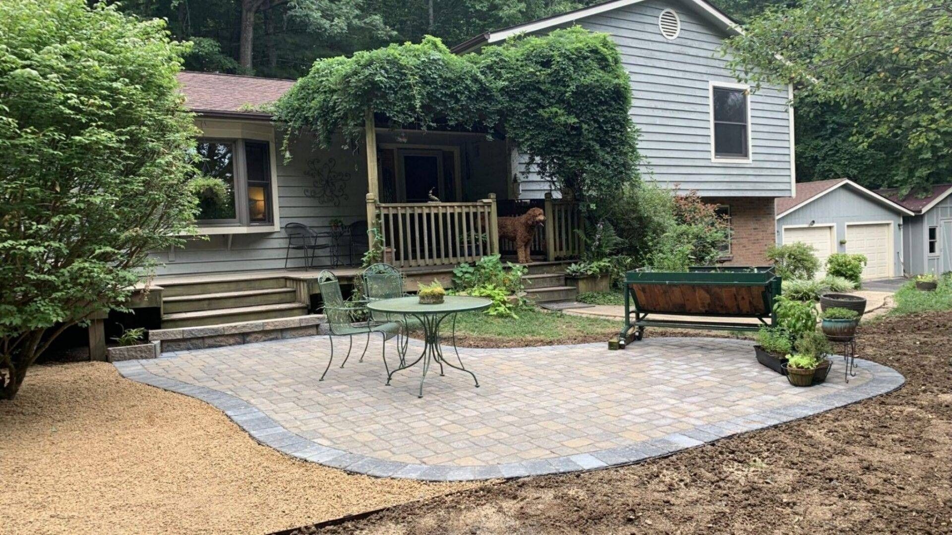 Backyard patio with stone seating area, potted plants, and a house with a porch and deck across the yard
