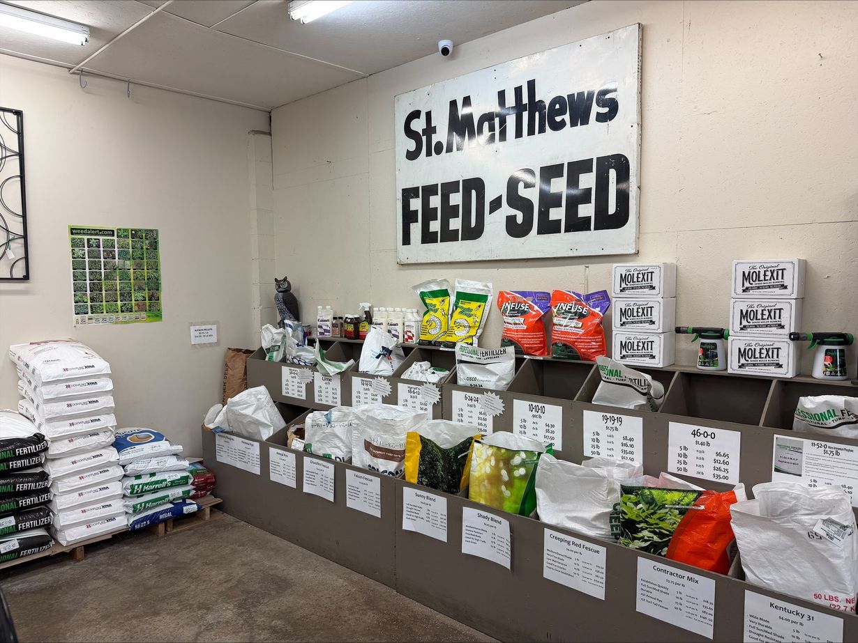 Feed and seed store display with stacked sacks, pet food bags, and a “St. Matthew’s Feed & Seed” sign.