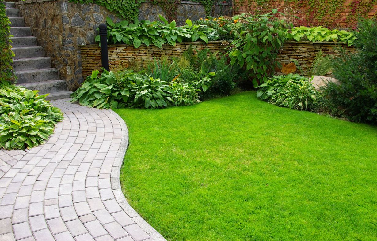 Curved stone path beside a lush green lawn and stone steps in a garden.
