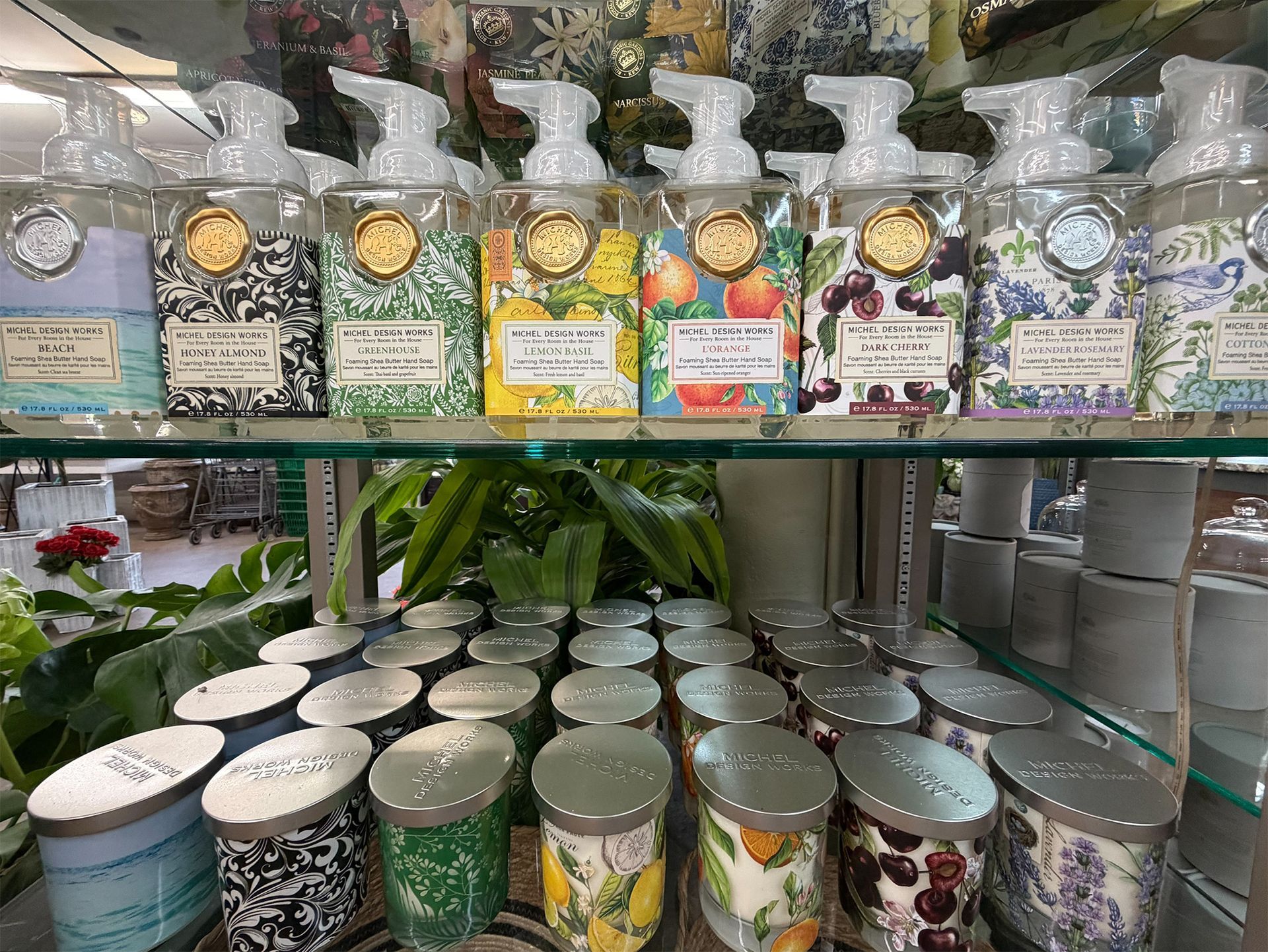 Shelf of assorted scented candles in glass jars with decorative labels and lids, displayed in a store.
