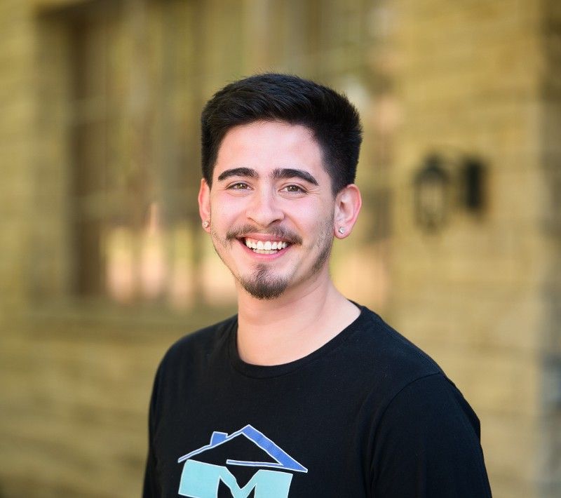 Conner Mendoza wearing a black shirt with a house on it is smiling for the camera.