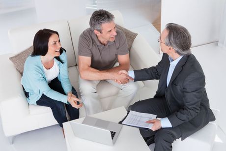 A man and woman are shaking hands with a man in a suit while sitting on a couch.
