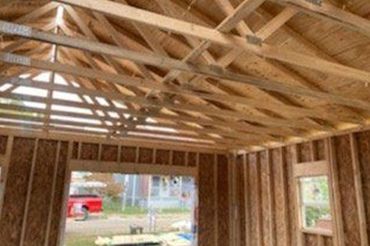 Interior of a framed house under construction with exposed wooden roof trusses and open wall studs.