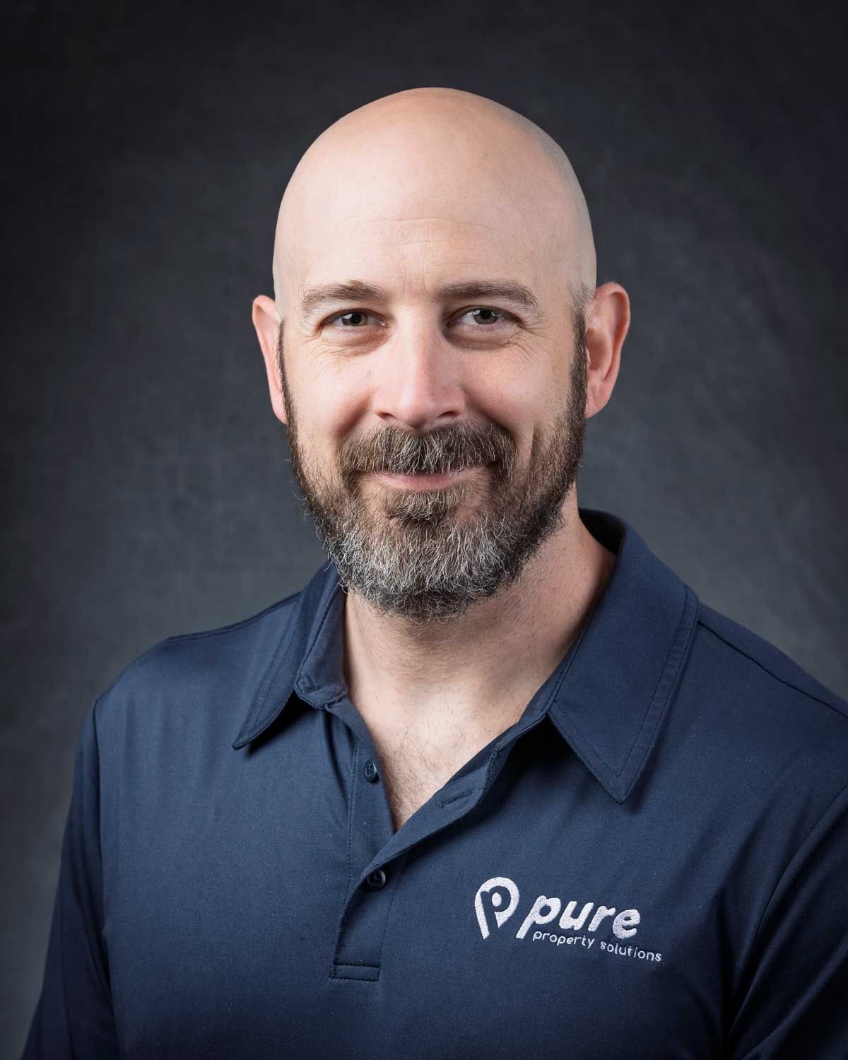 Bald man with beard wearing a blue polo shirt with 