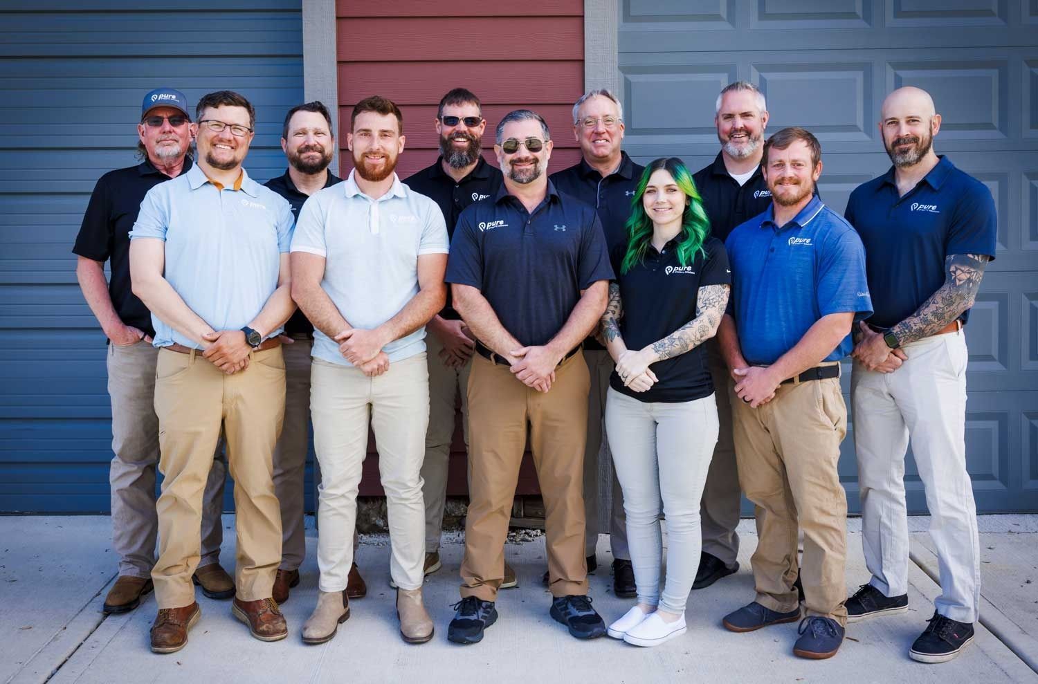 Group of 12 people smiling in front of a building. Several are wearing company shirts,.