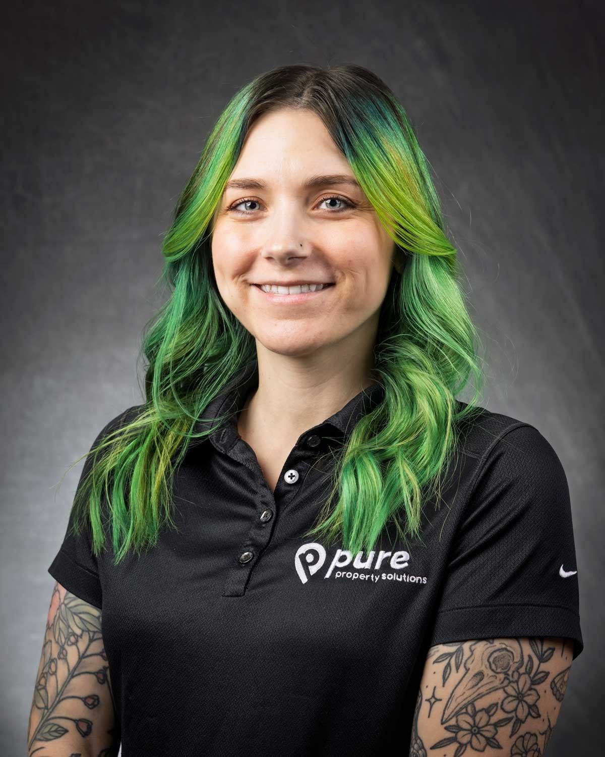 Woman with green hair, smiling, wearing a black polo shirt with 