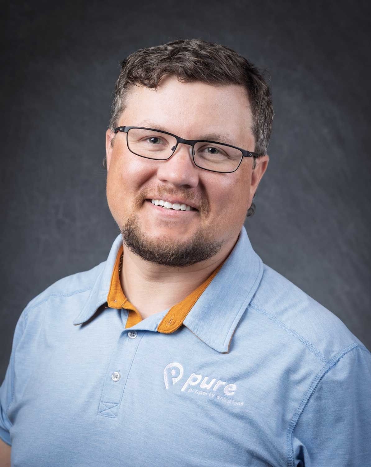 Man with glasses smiling, wearing a blue polo shirt with 