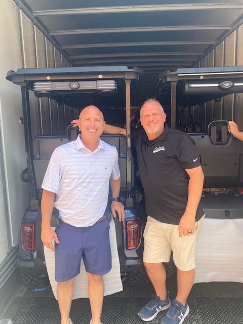 Two men are standing in front of a golf cart