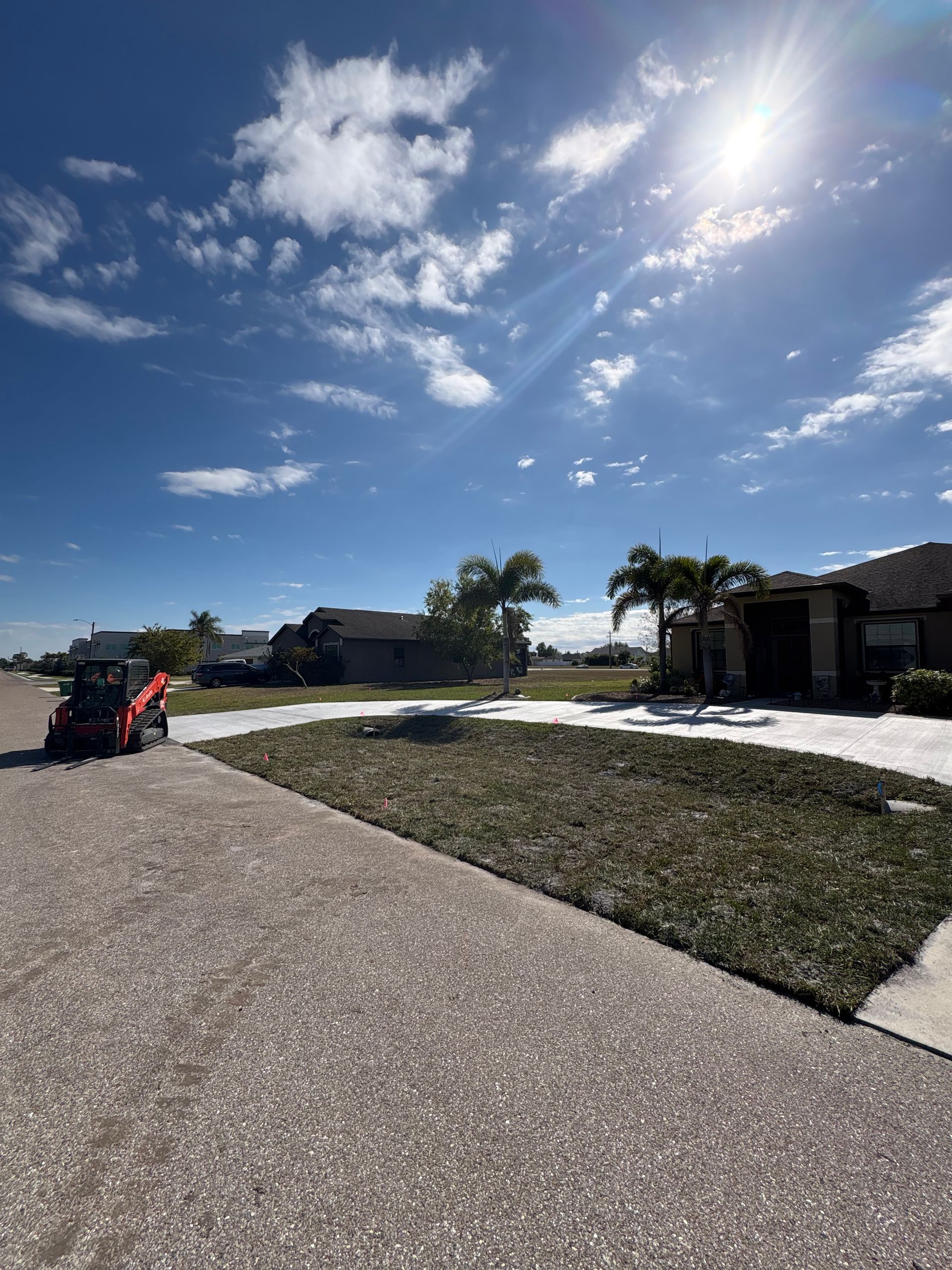 A lawn being mowed next to a street under a bright blue sky. A small orange mower is in the shot.