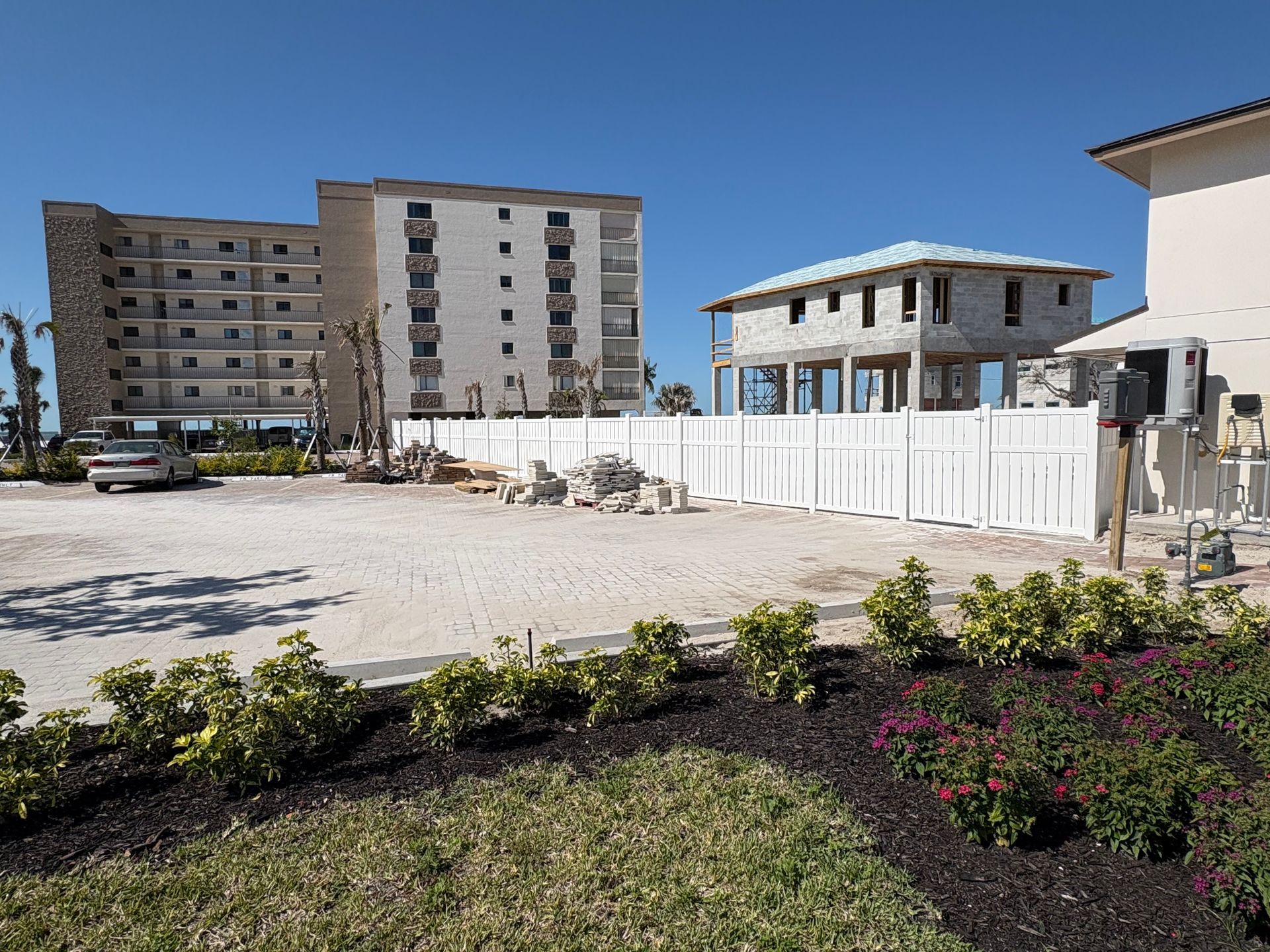 Construction site with buildings and a white fence. Brown earth, blue sky.