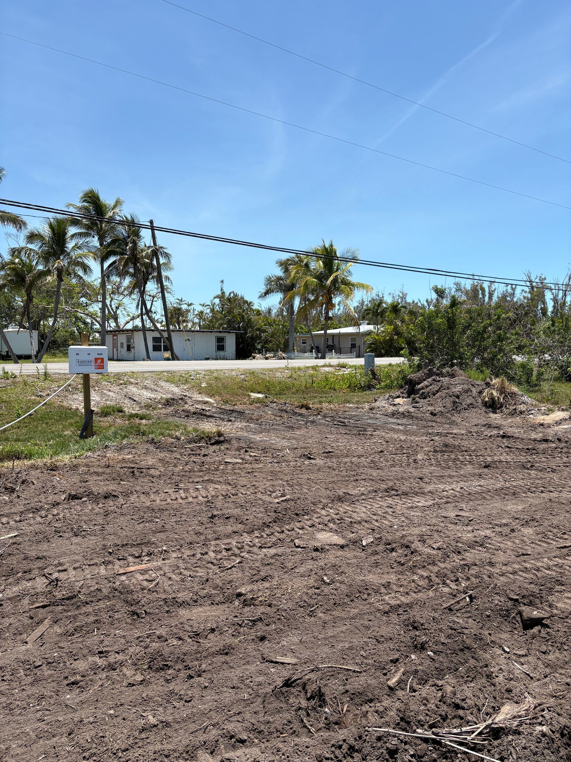 Dirt lot with a mailbox and several low buildings under a blue sky with palm trees.