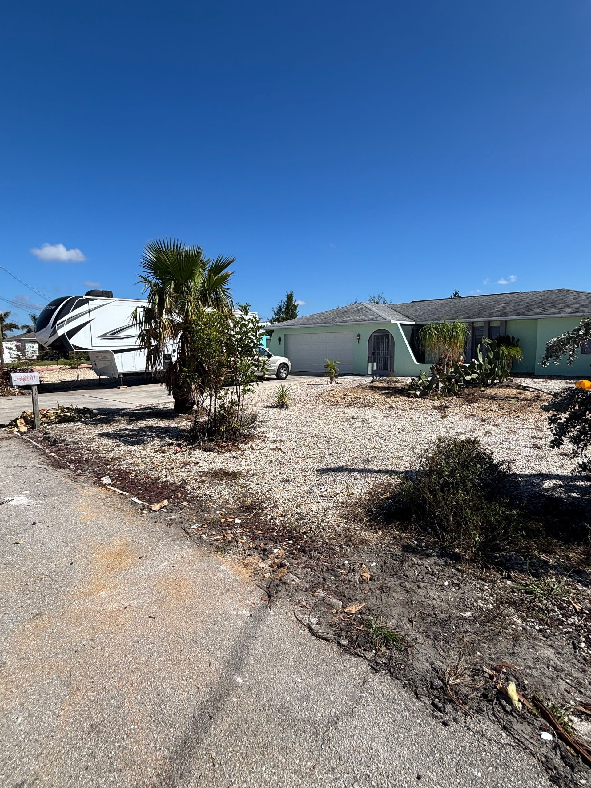 Damaged houses and a boat, showing hurricane aftermath. Debris scattered on ground under a blue sky.
