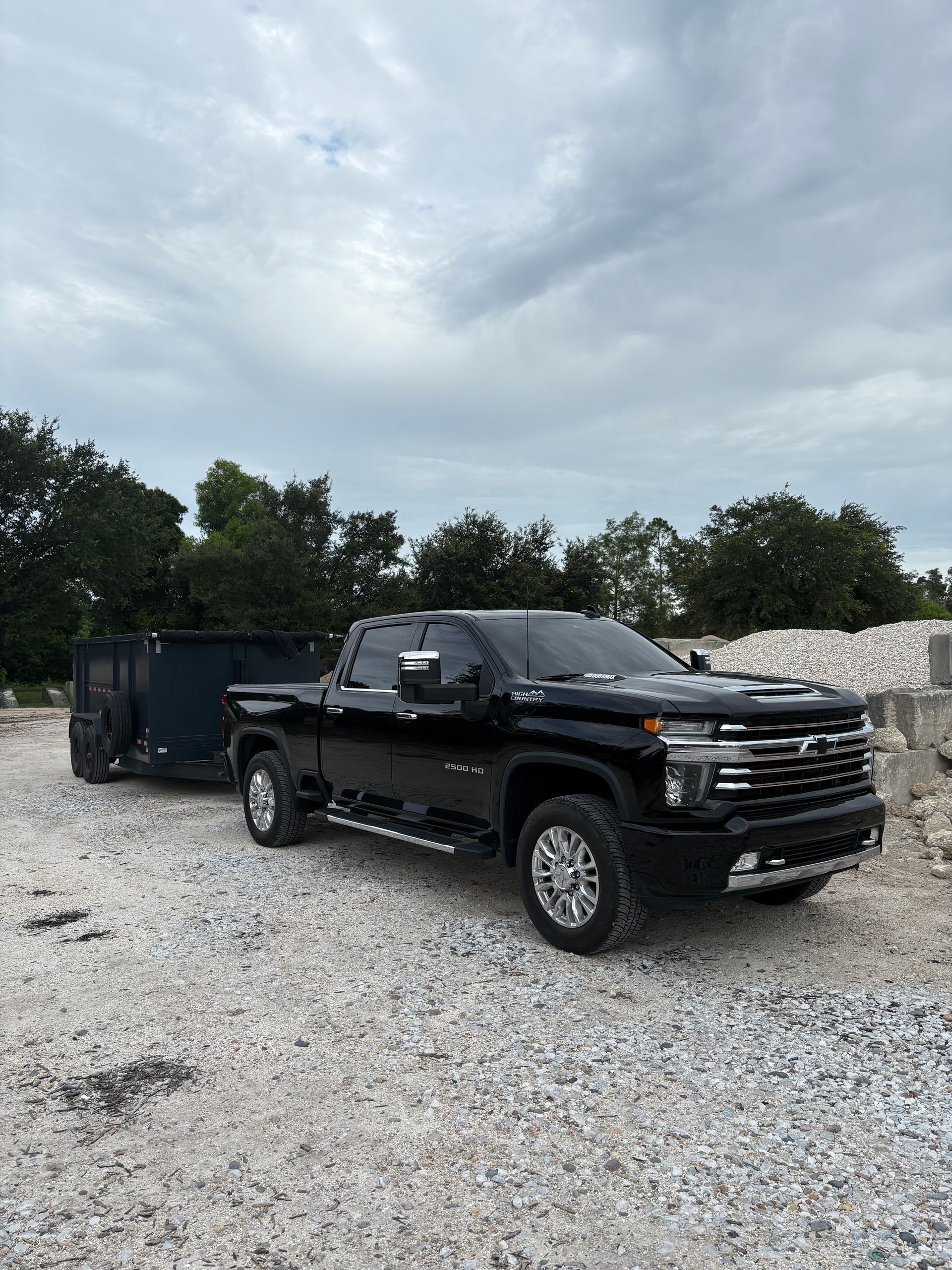 Black pickup truck towing a trailer on a gravel lot under a cloudy sky.
