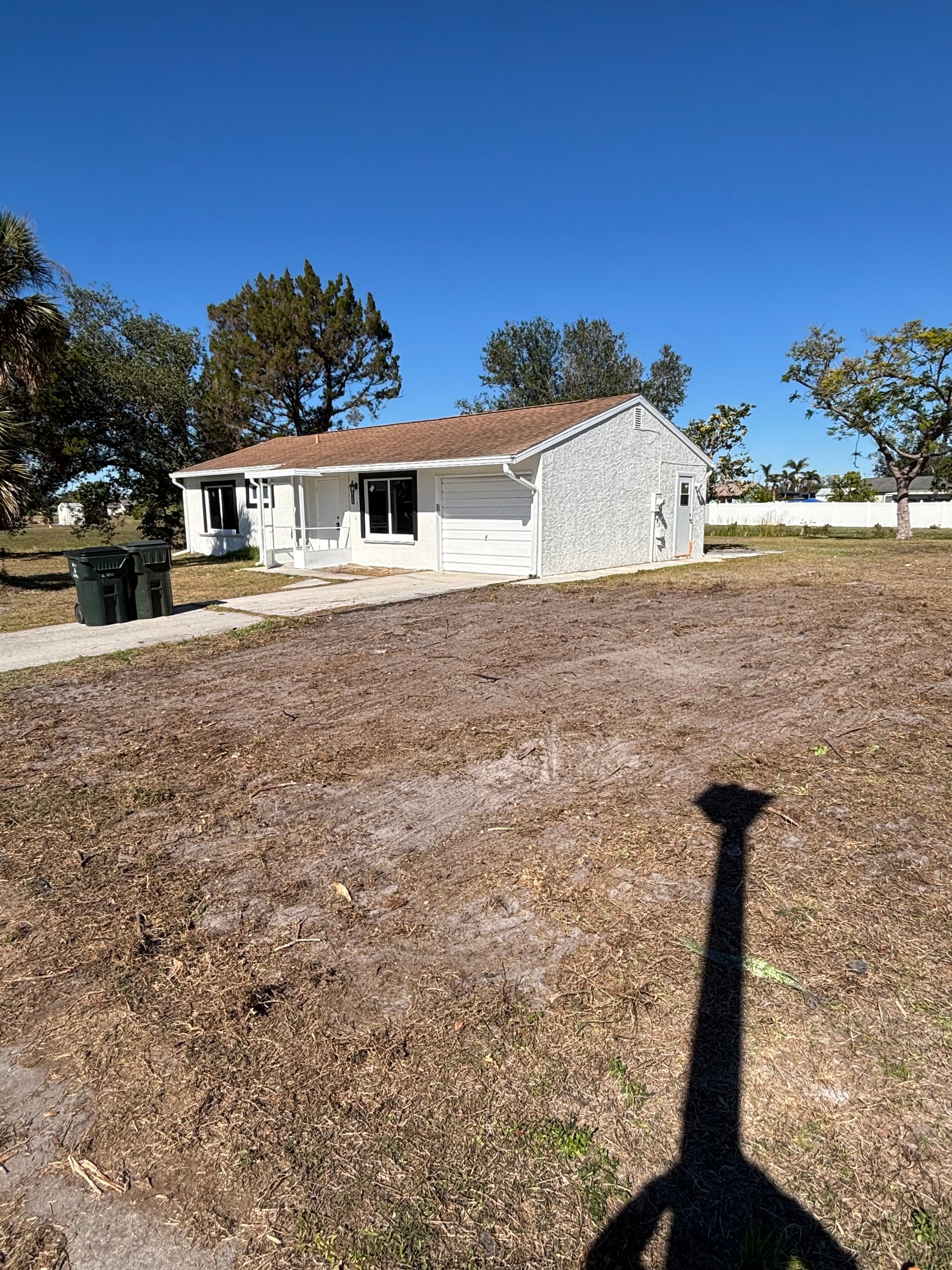 Single-story house with brown roof and white siding, on a dry, brown lawn under a blue sky.