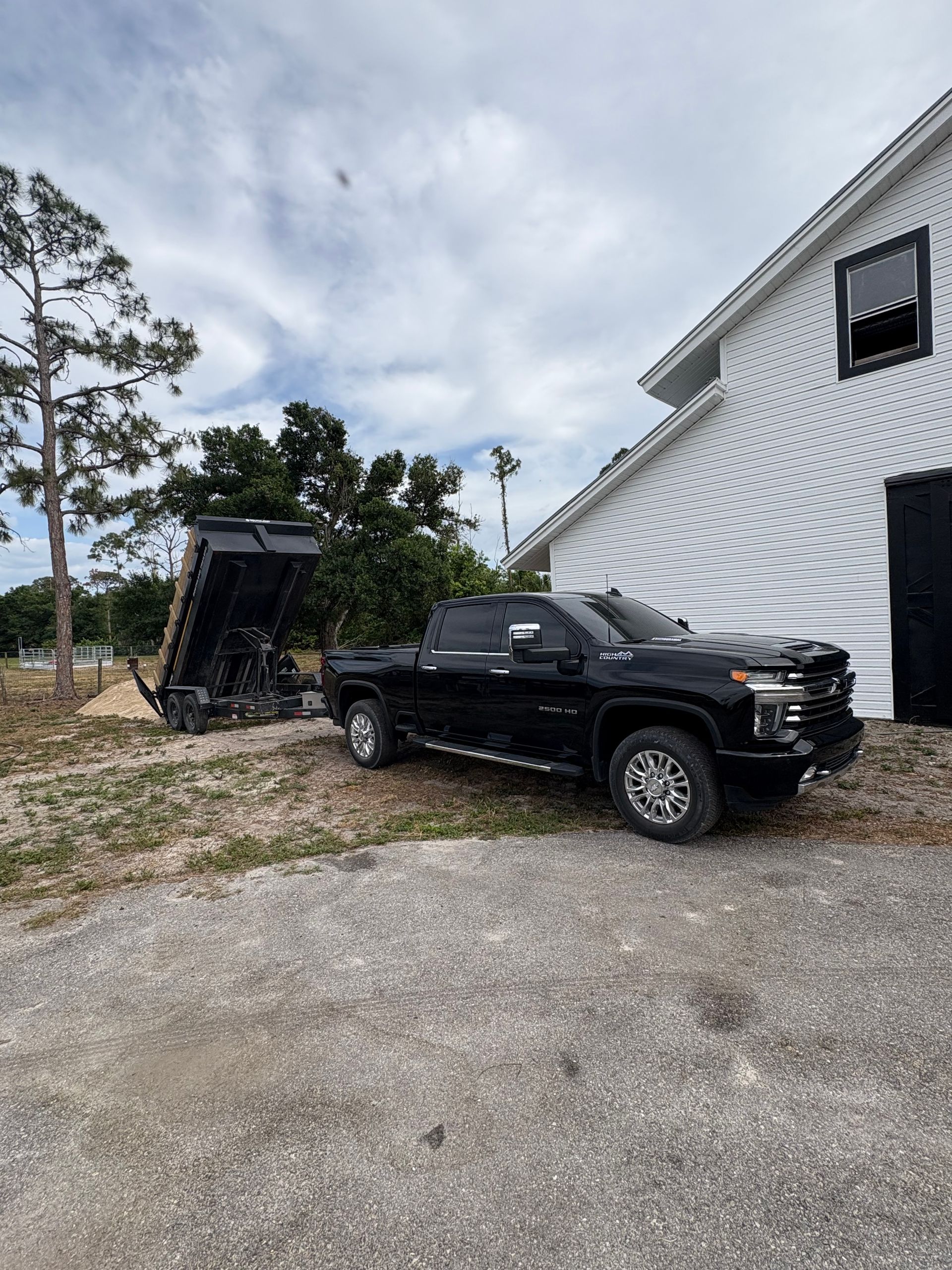 Black pickup truck with a raised dump trailer parked next to a white building under a cloudy sky.