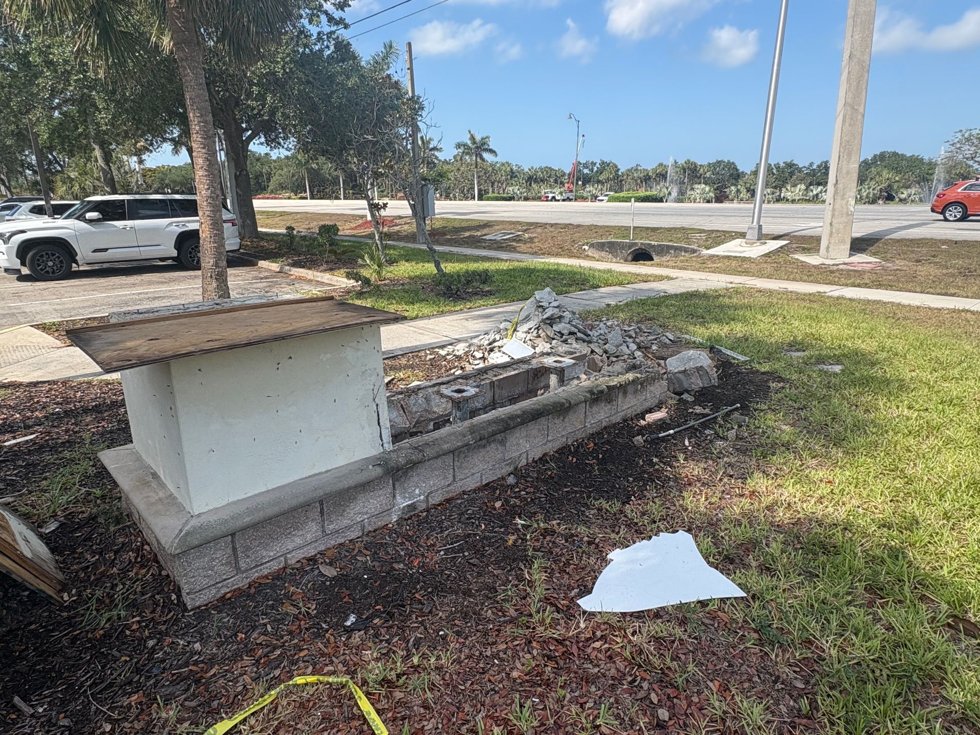 White box on a brick base, next to a broken concrete structure and grass on a sunny day.