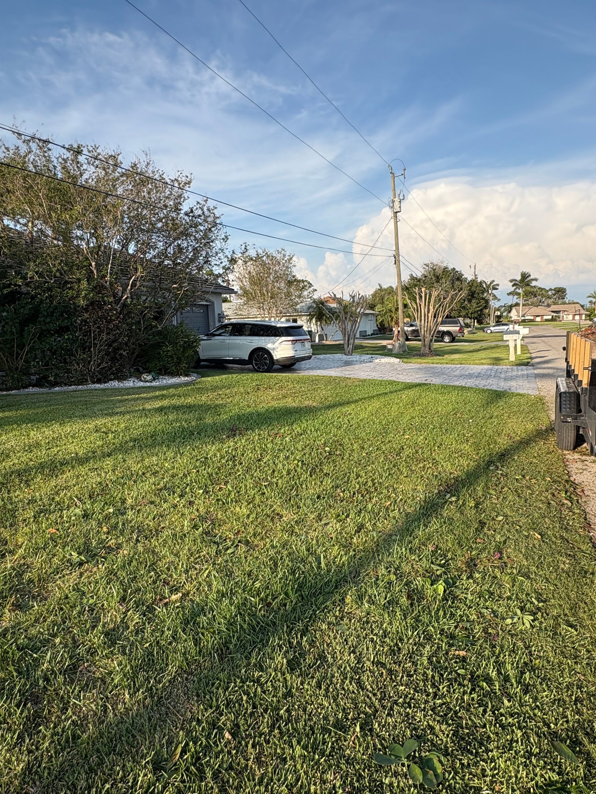 A white vehicle parked in a driveway. Green grass in the foreground under a cloudy blue sky.