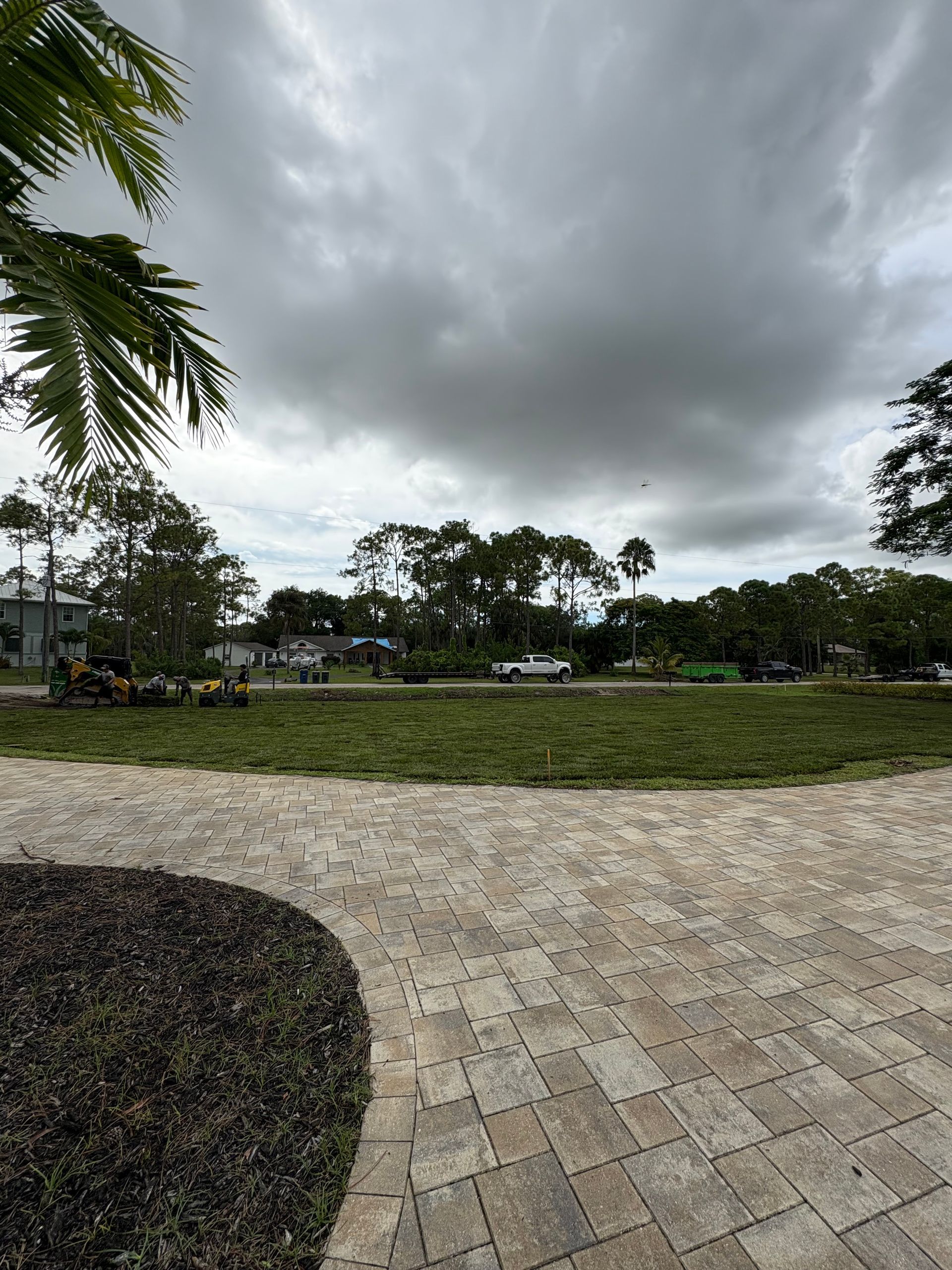 Paved path leading to a grassy area with trees, under a cloudy sky.