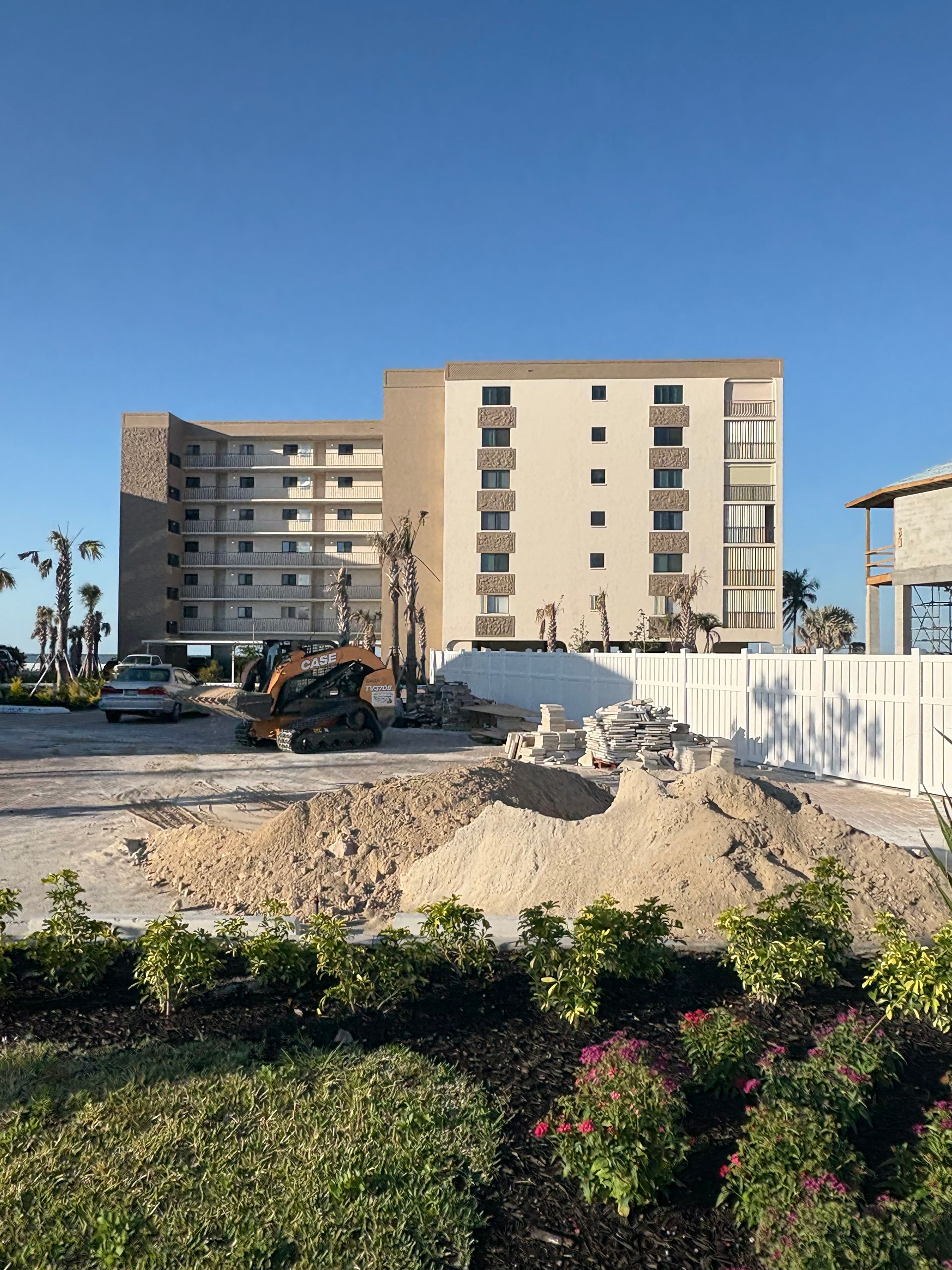 Construction site in front of a multi-story building.  A pile of dirt and machinery is visible. Bright sky.