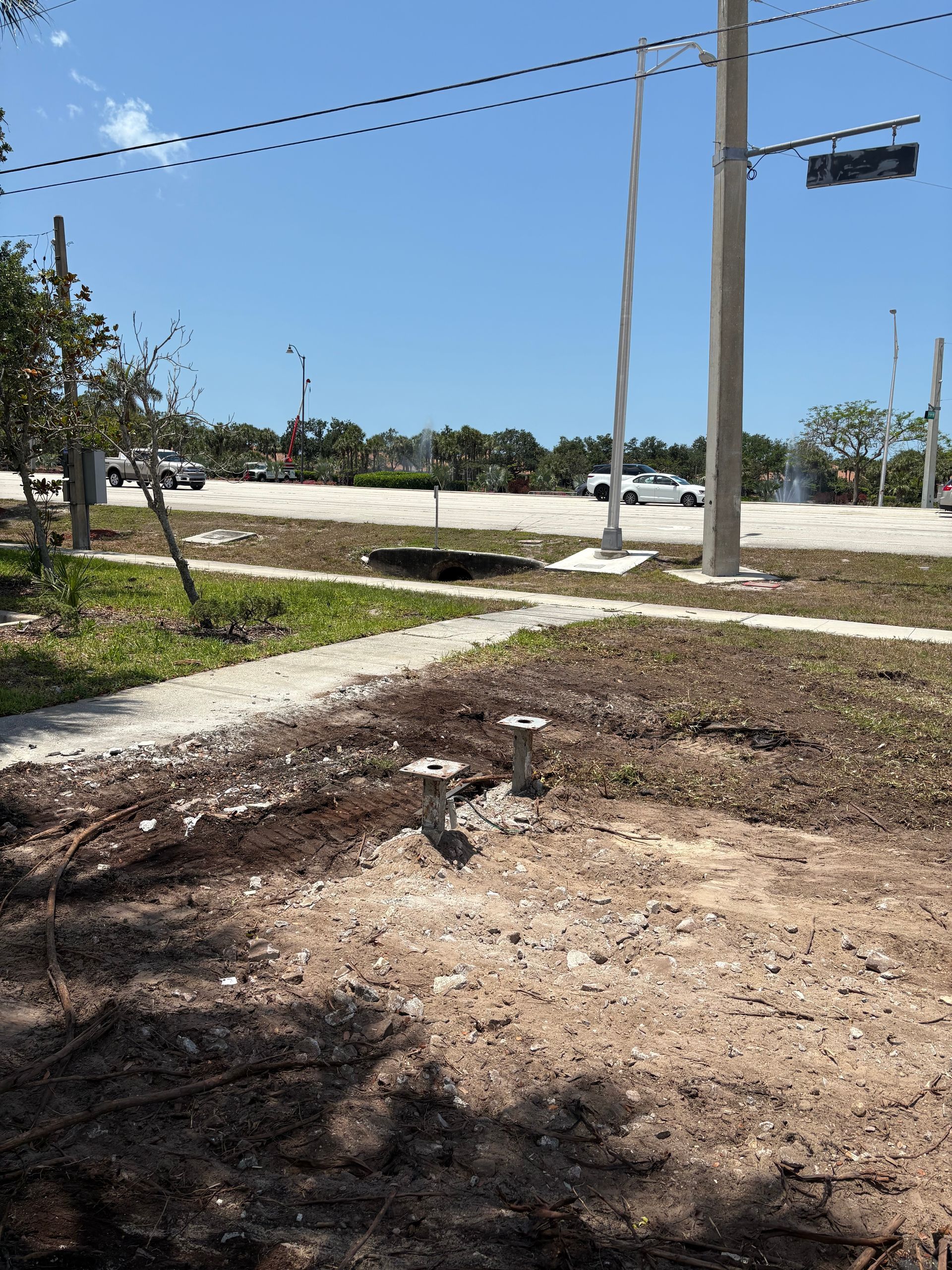 Grassy area with sidewalk, utility poles, and road in the background under a blue sky.