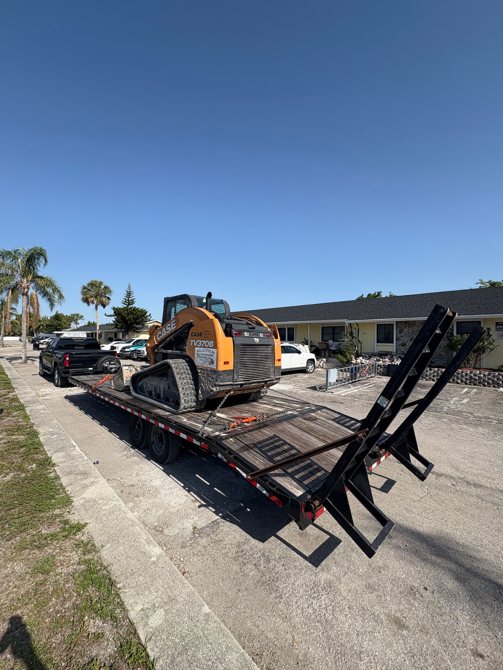 Skid steer loader on a trailer in front of a house on a sunny day.
