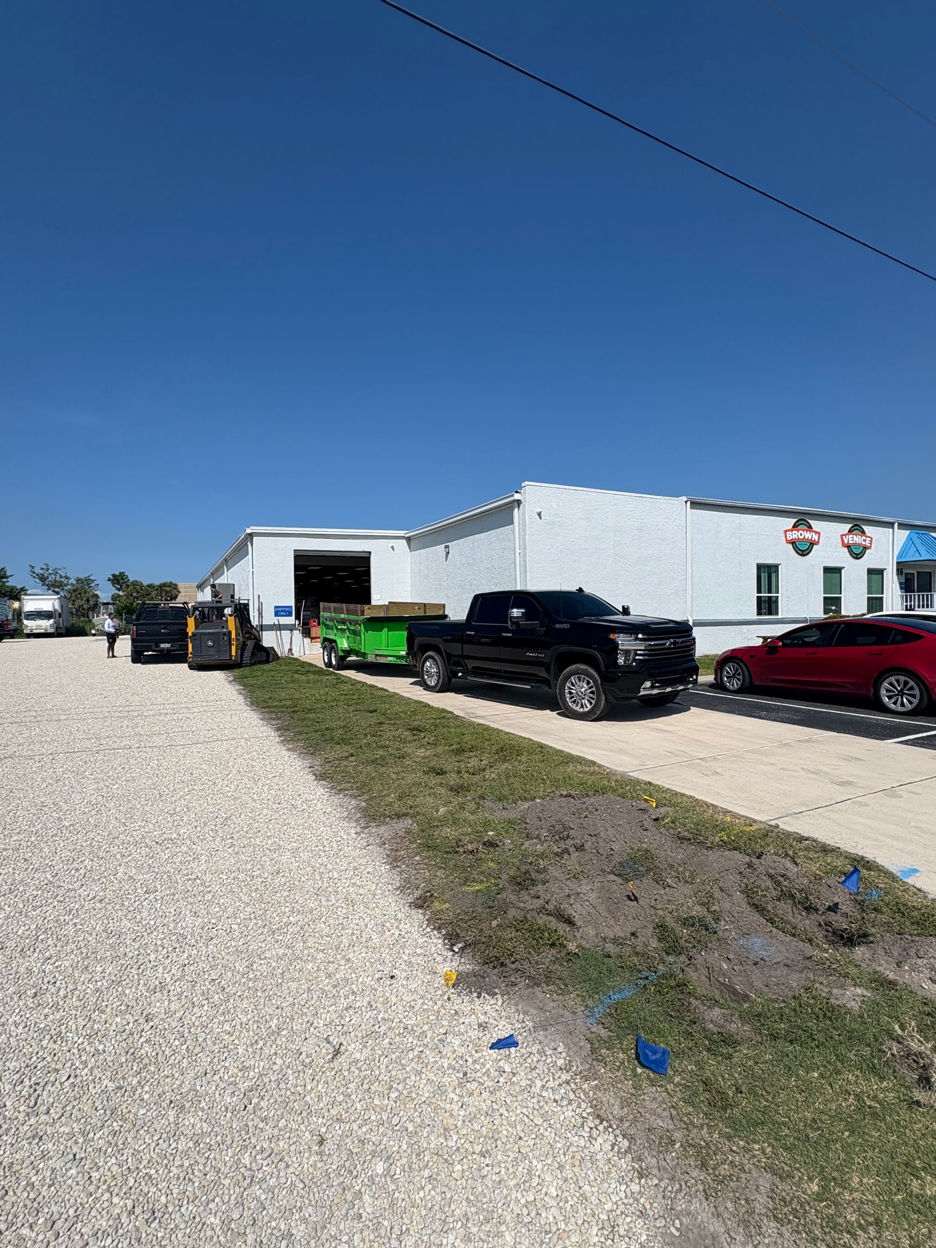 Black pickup truck and trailer parked near white building under a clear blue sky.