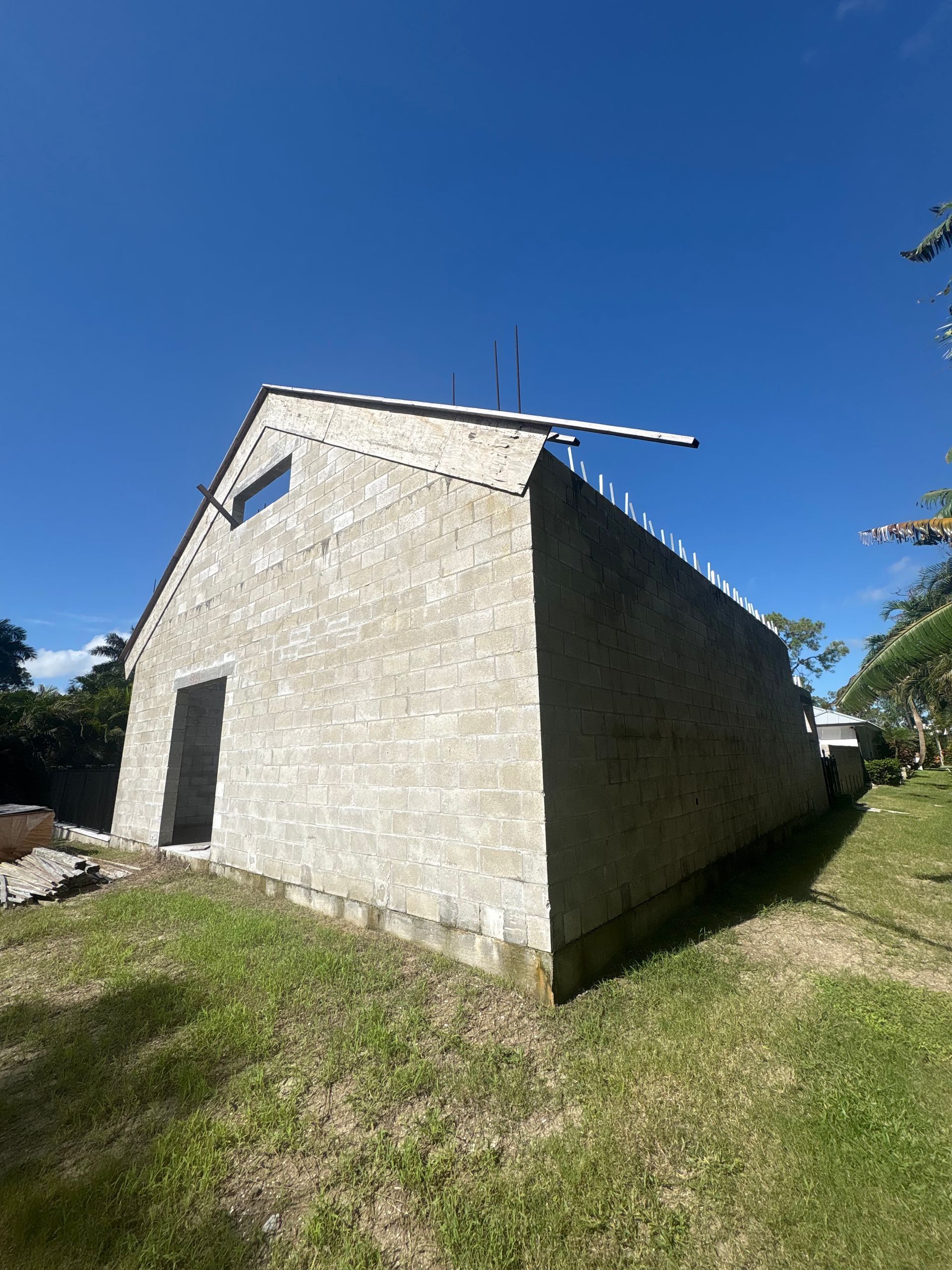A partially constructed concrete building with a gable roof, under a blue sky.