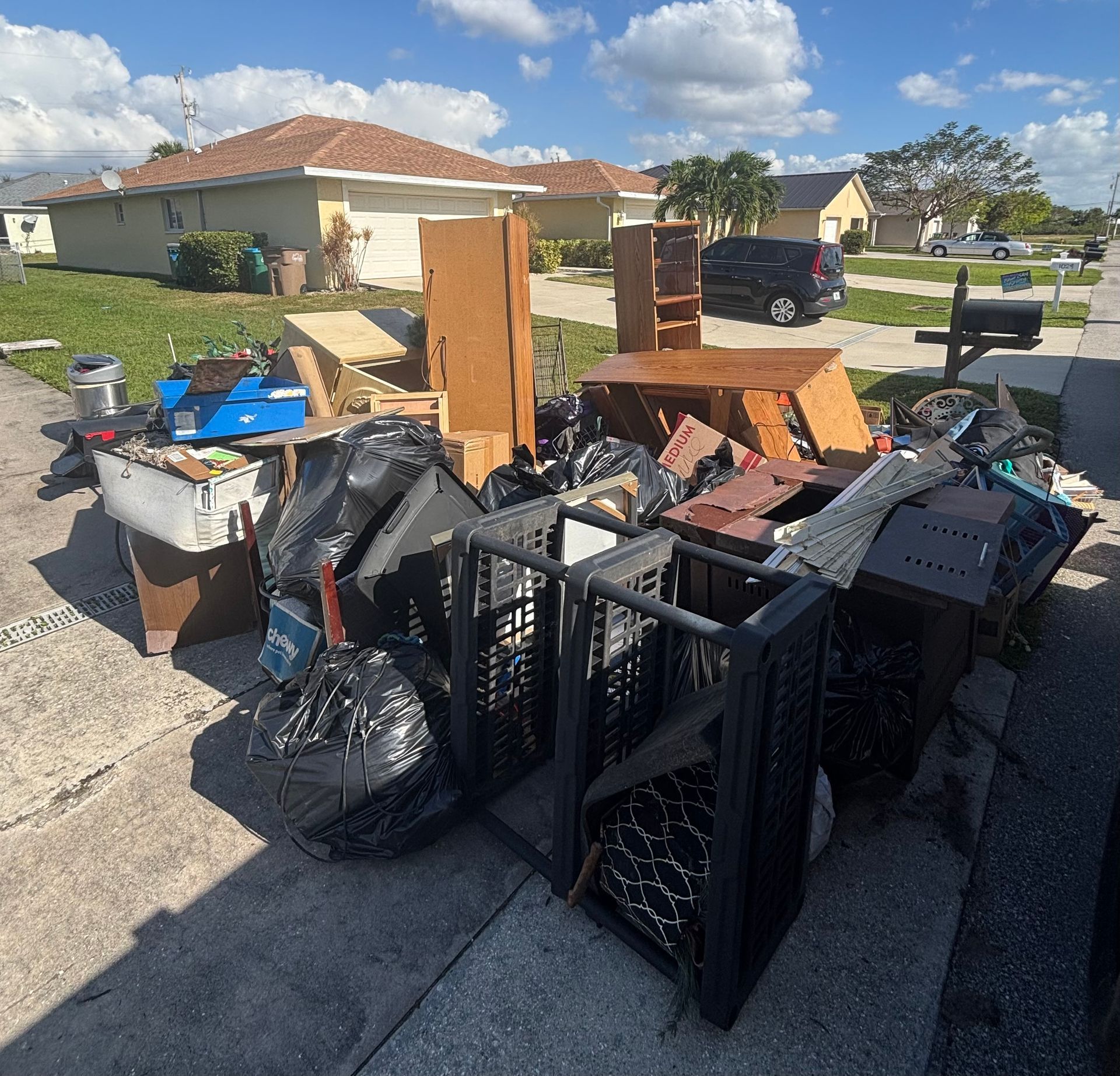 Pile of discarded furniture and trash on a residential curb, including wooden cabinets and black trash bags.