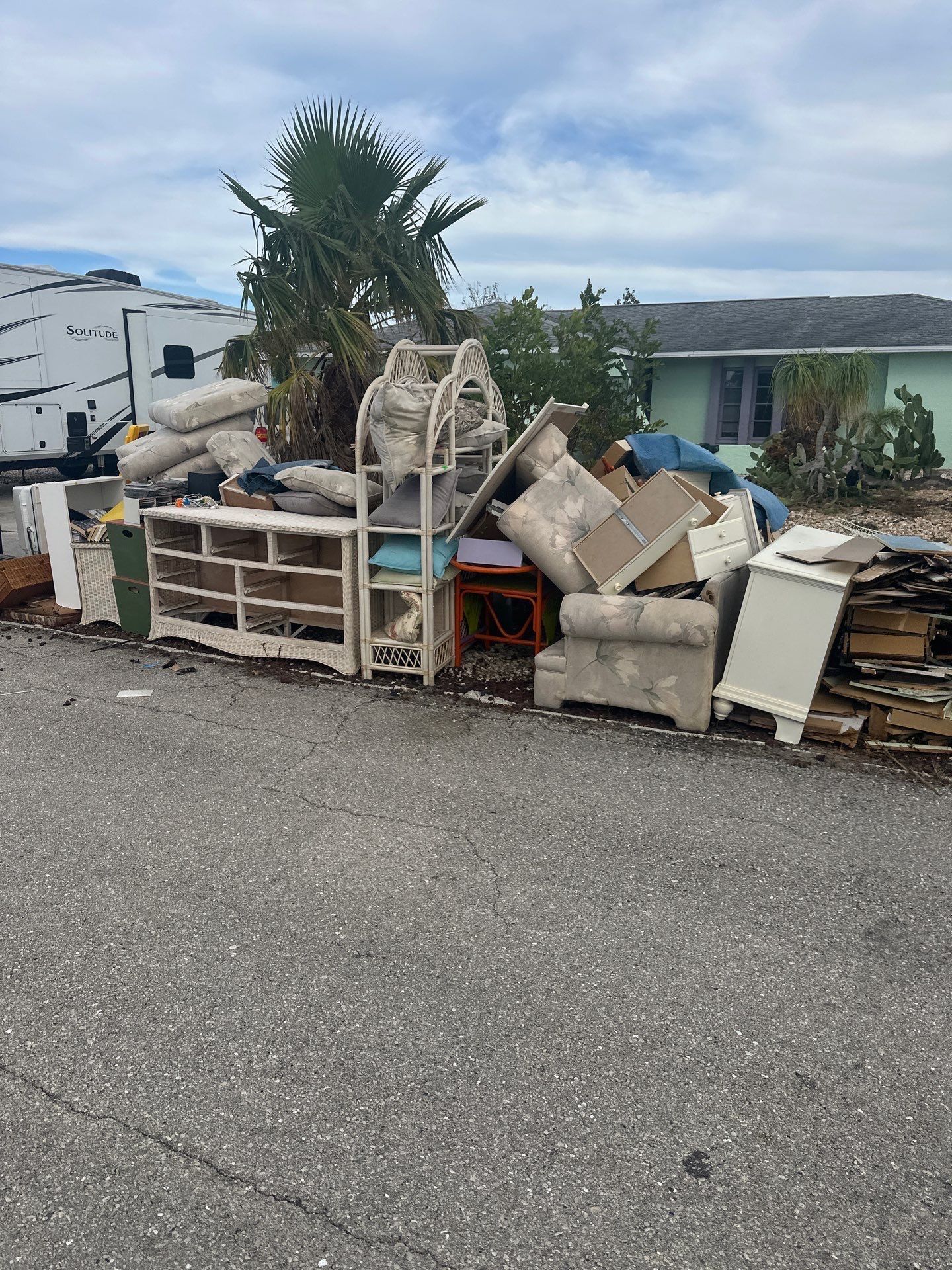 Pile of debris, including furniture, on a road. A house and RV are in the background under a cloudy sky.