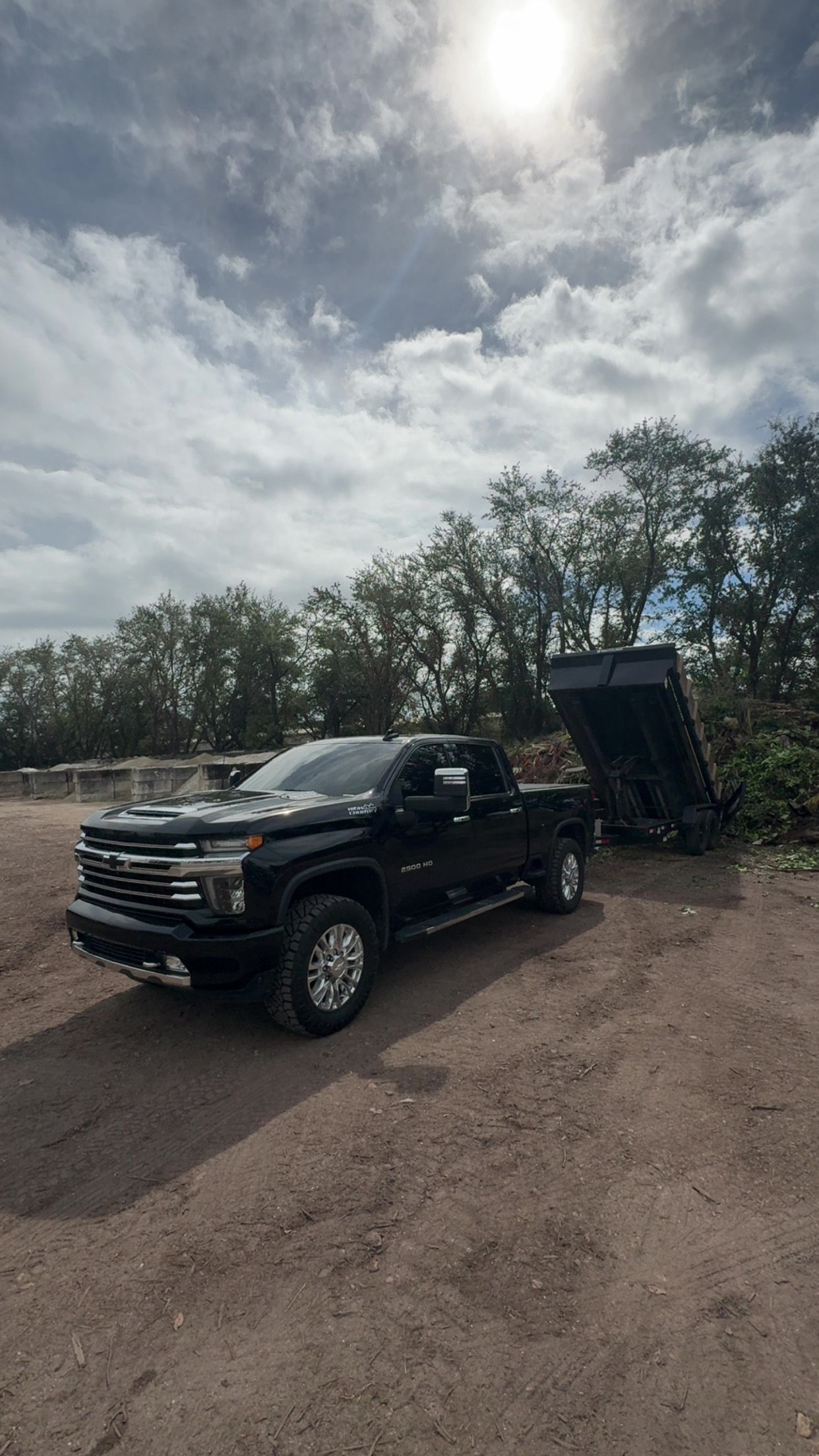 Black pickup truck with trailer on dirt road under a cloudy sky.
