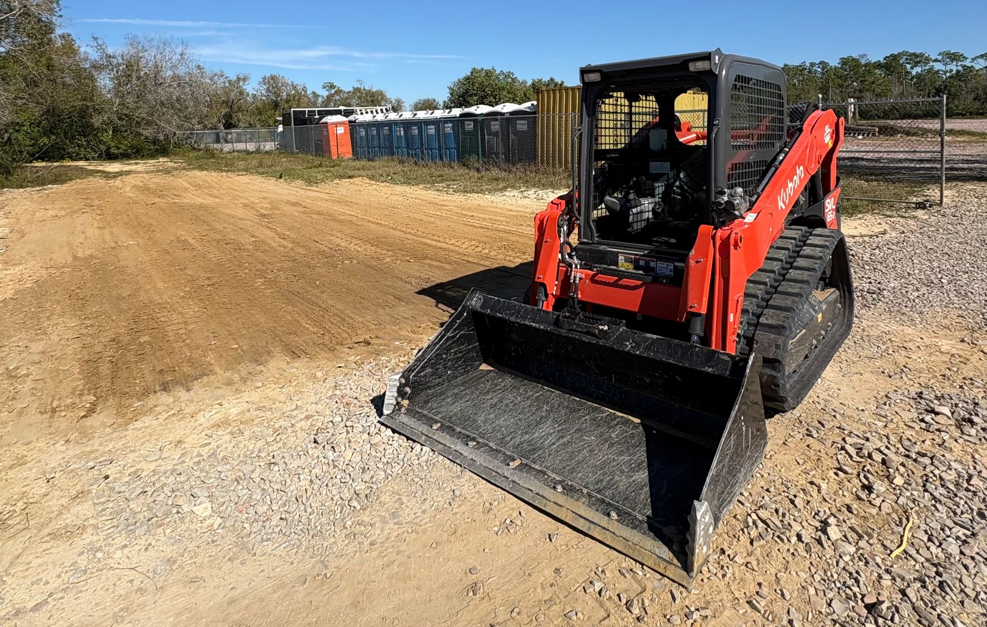 Red track skid steer loader on a construction site with blue sky in the background.