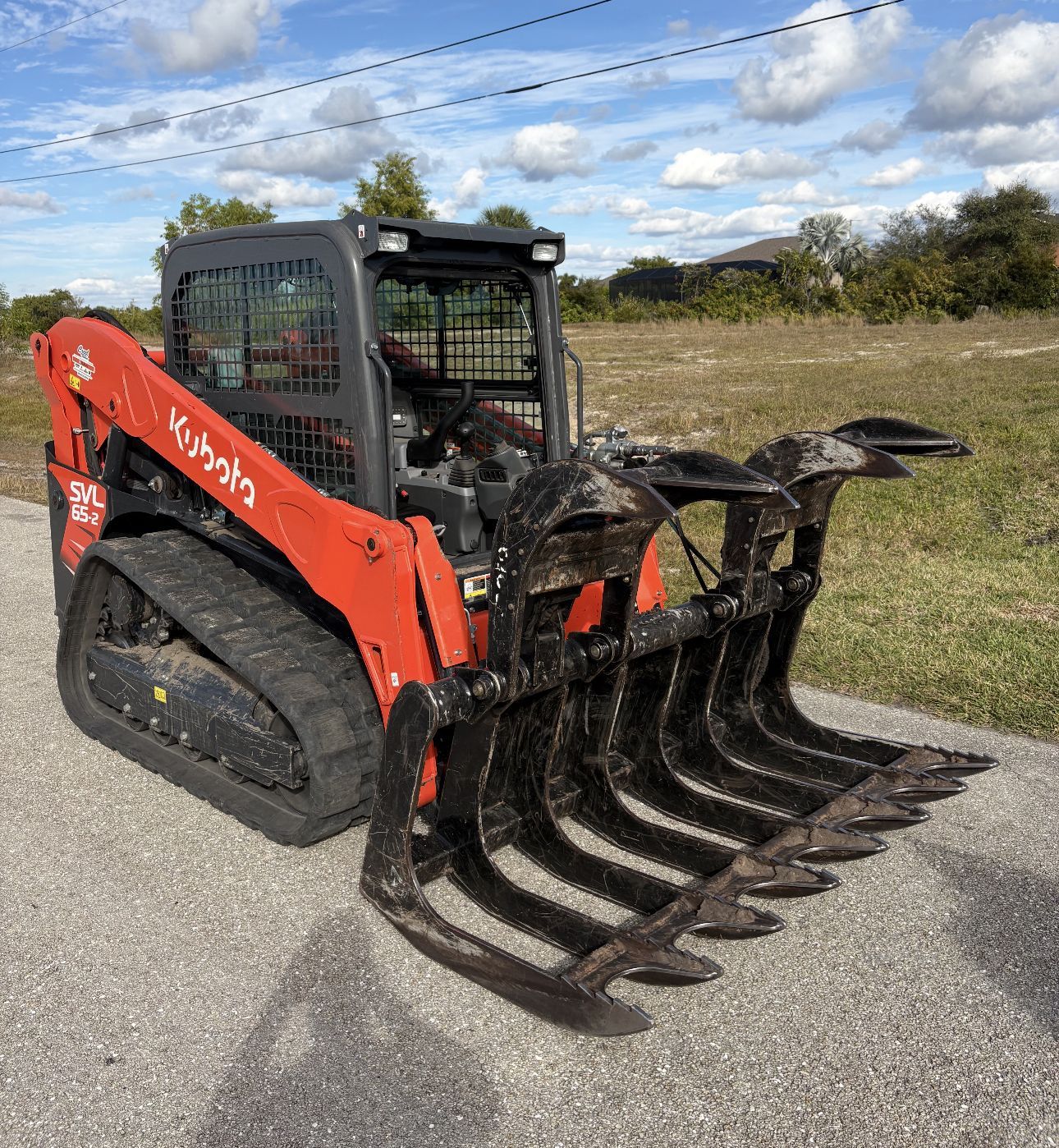 Orange and black Kubota track skid steer with grapple attachment, outdoors.