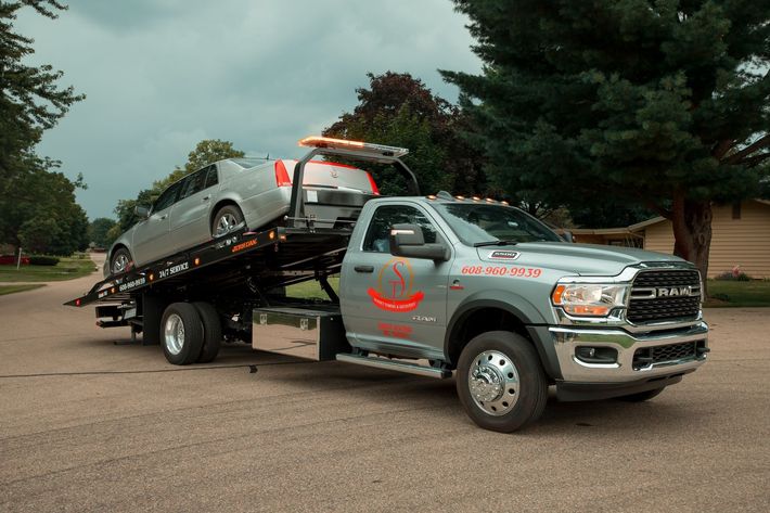 A tow truck is carrying a car on the back of it. 