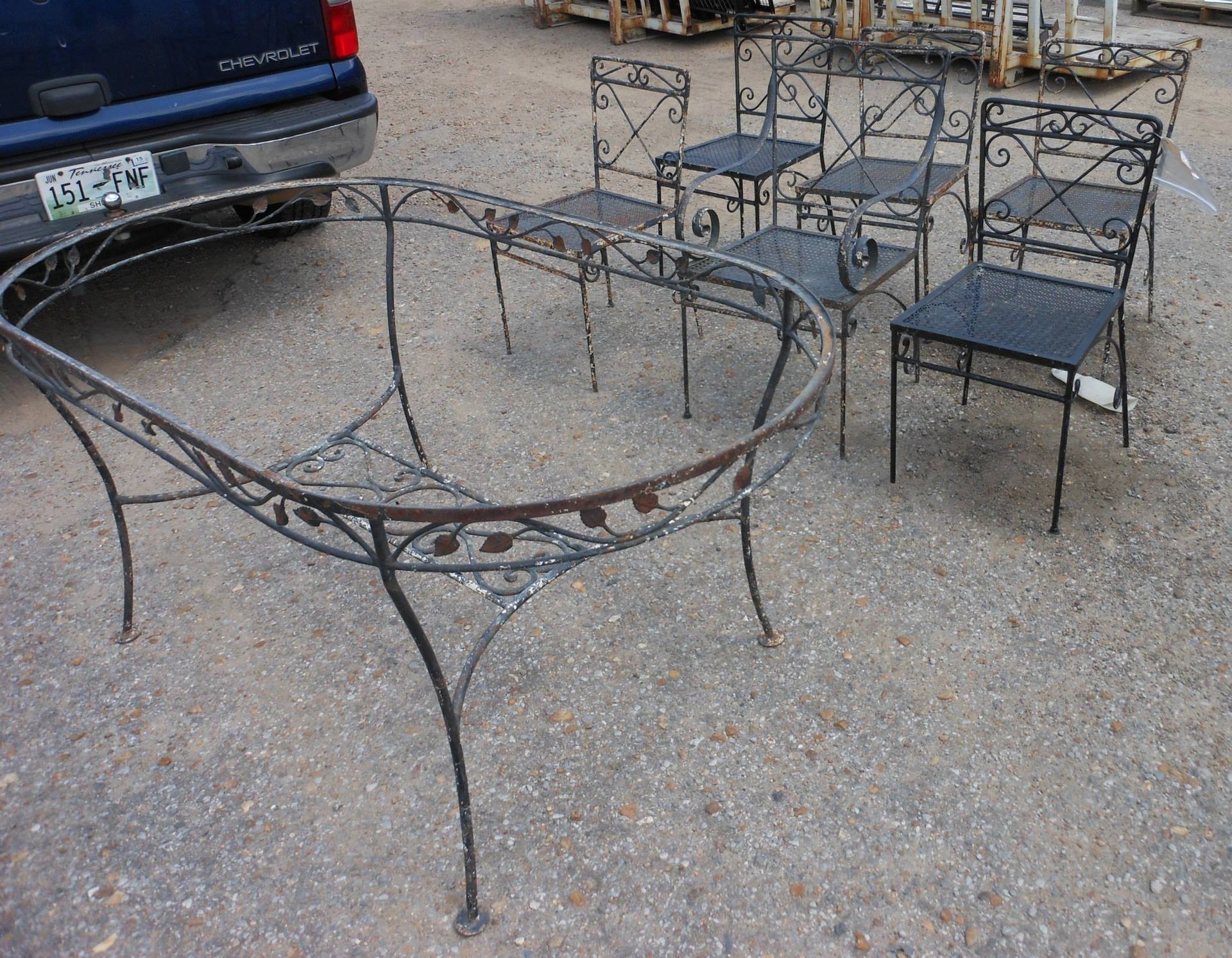 Wrought iron patio table and chairs on gravel beside a blue truck.