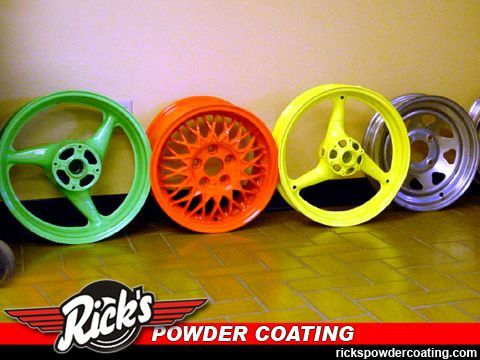 Four colorful car wheels: green, orange, yellow, and silver rims on a tiled floor with Rick’s Powder Coating logo.
