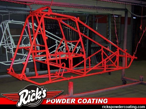 Red powder-coated tubular race car chassis in a workshop, with Rick’s Powder Coating logo.