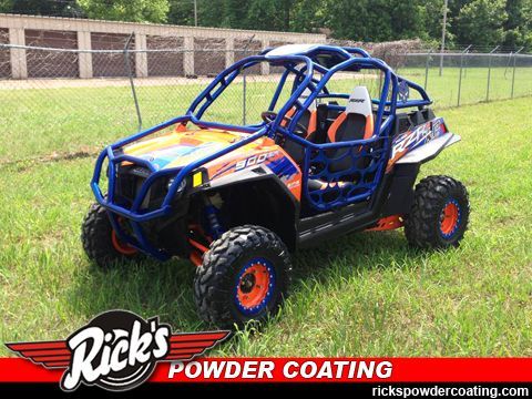 Blue and orange off-road buggy with roll cage and orange wheels on grass, with Rick’s Powder Coating logo