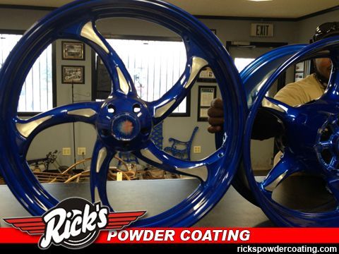 Blue powder-coated car rims displayed in a shop with Rick's Powder Coating logo.