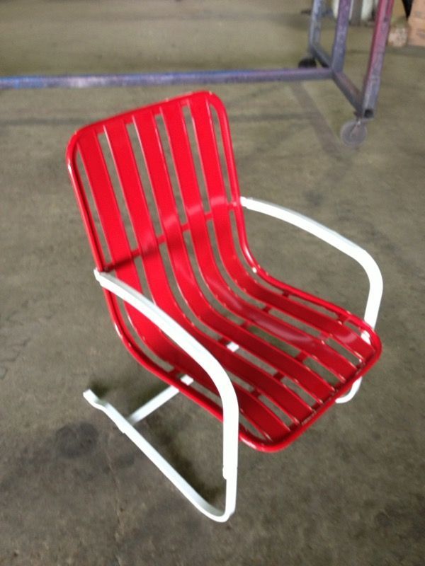 Red slatted metal chair with white arms and legs on a concrete floor.
