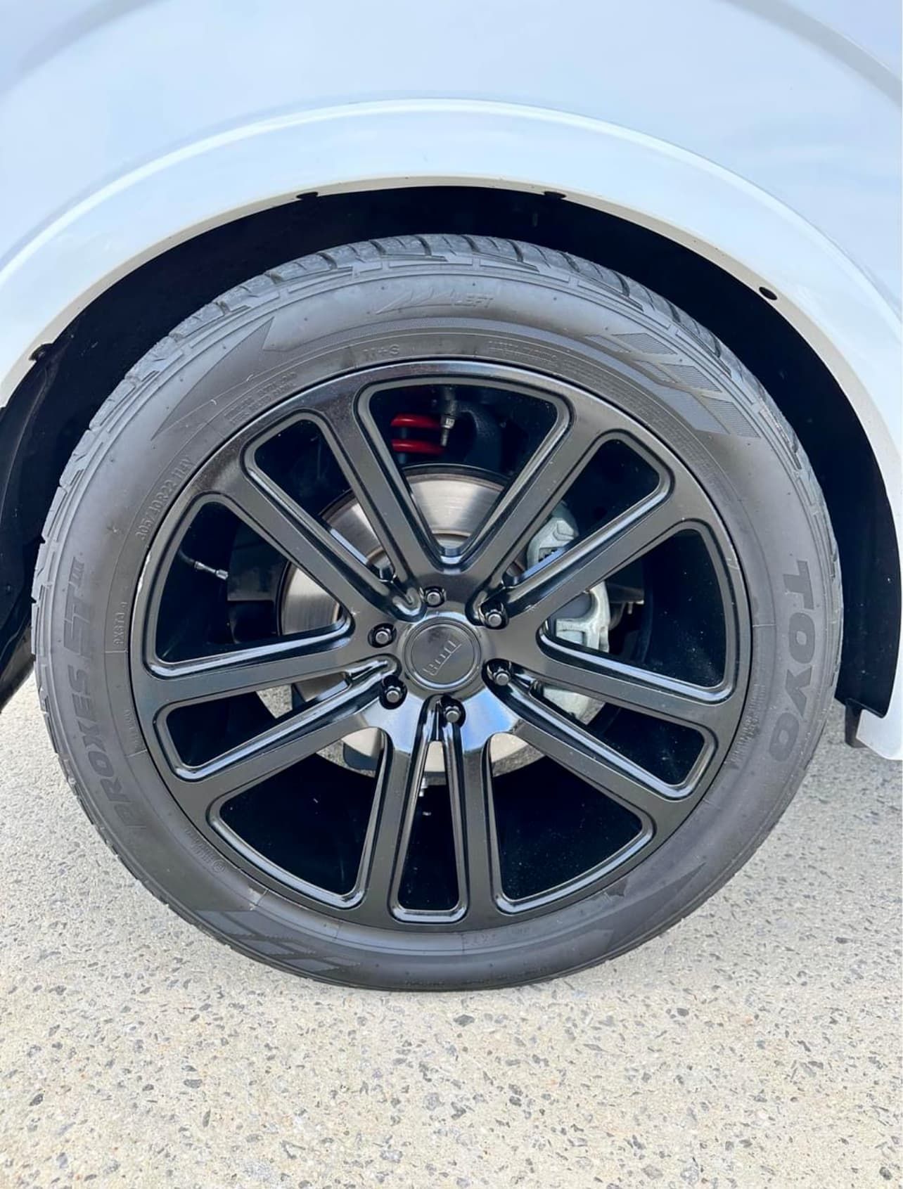 Close-up of a black alloy car wheel with tire under a white fender.